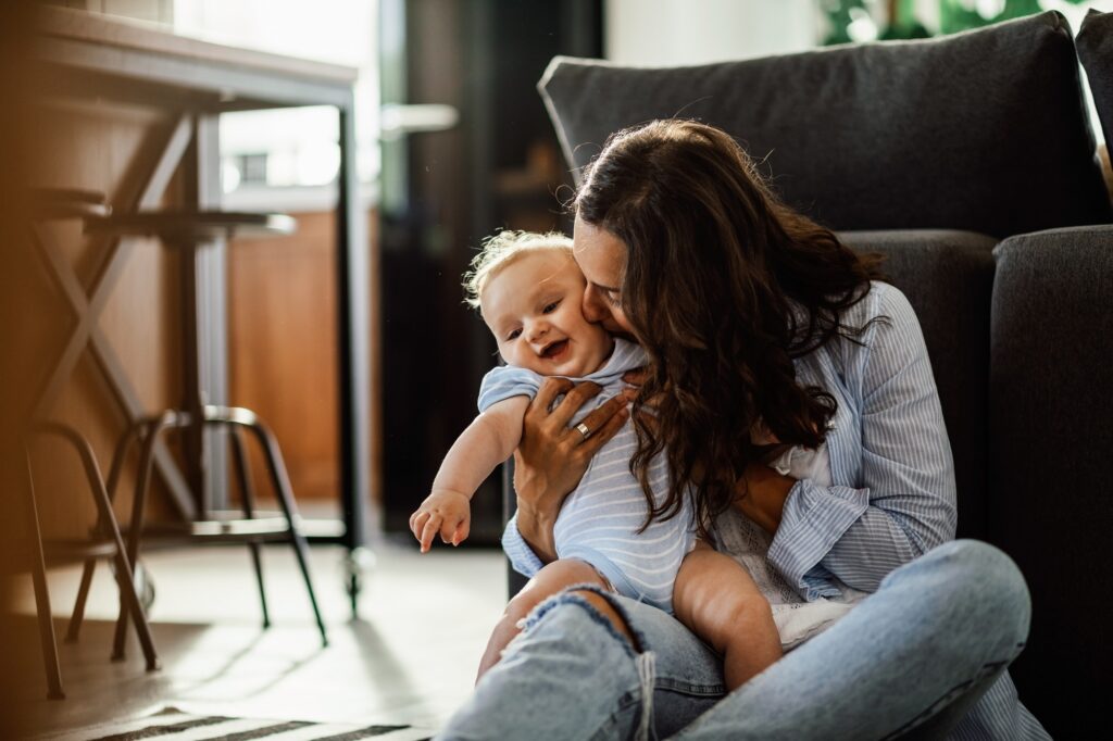 Happy baby being kissed by her mother at home.